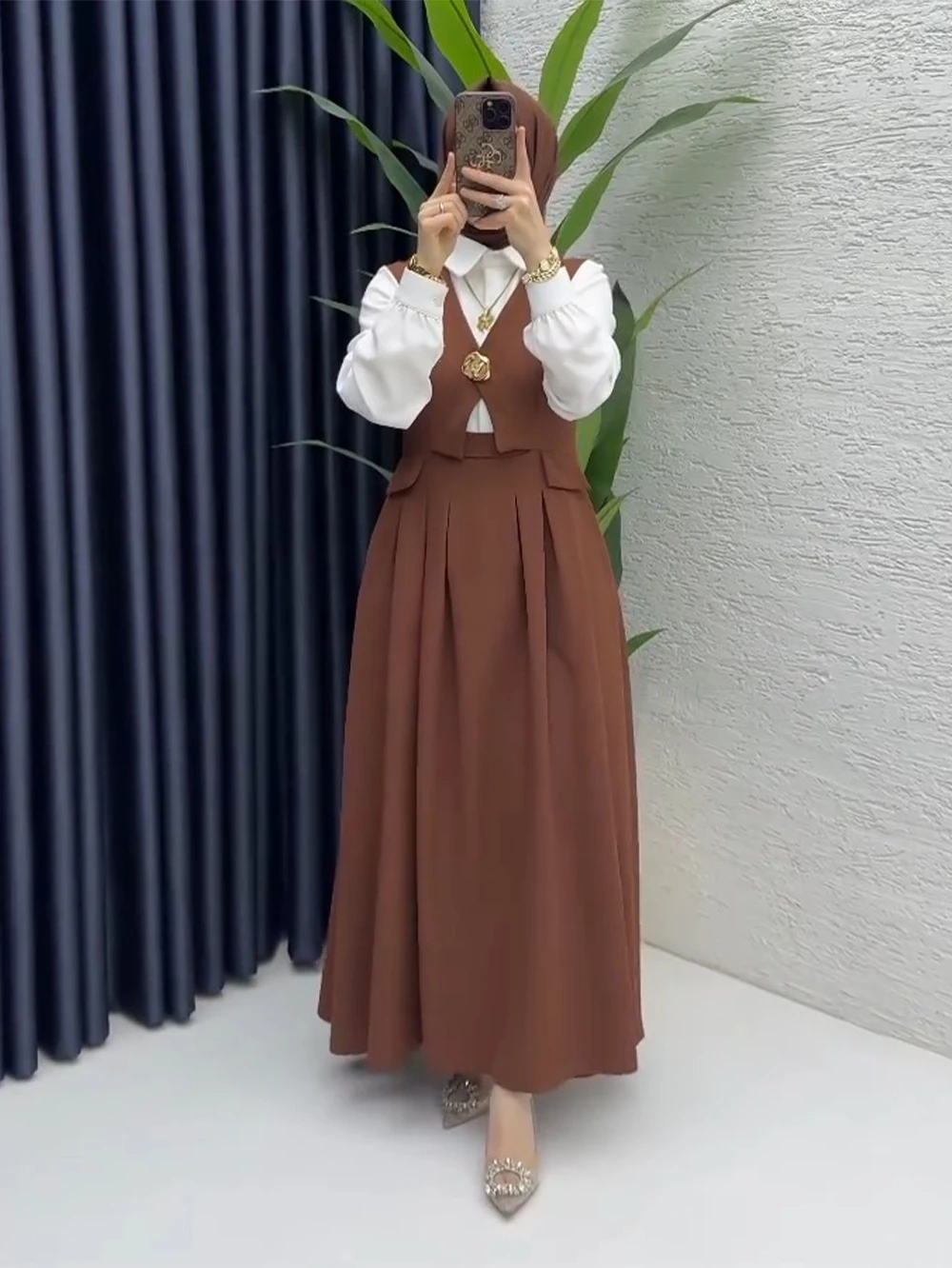 طقم نسائي كلاسيكي مكون من تنورة طويلة وصديرية باللون البني مع قميص أبيض.